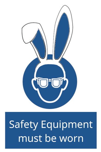 ISO 7010 standard warning sign with the caption "Safety Equipment must be worn". The sign shows a person's head in white against a blue background, with white text. The person is wearing glasses, or possibly safety goggles, and appears to have sprouted bunny ears.