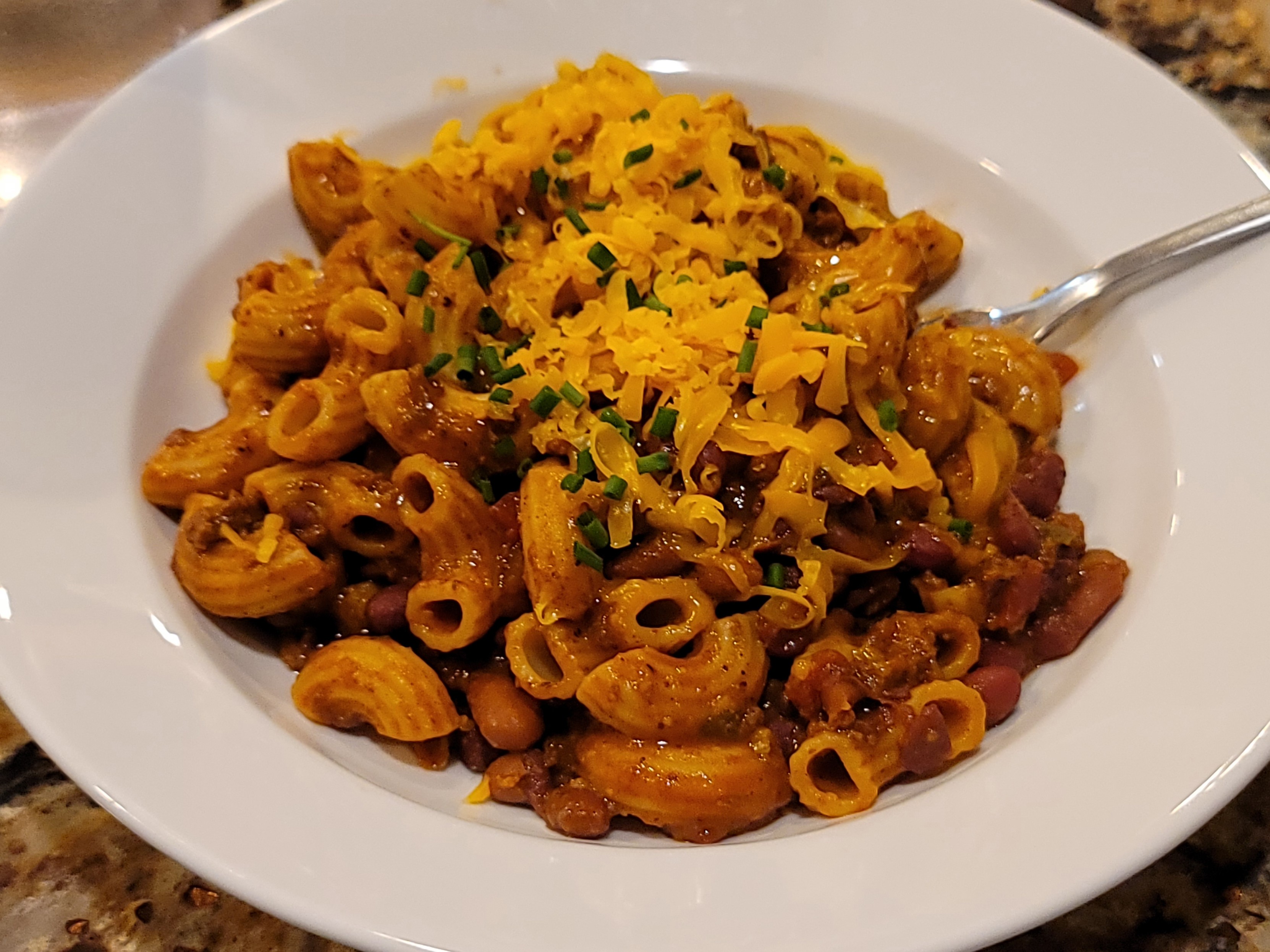 chili mac and shredded cheese in a white bowl