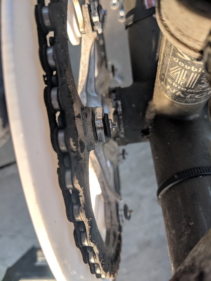Top view of a bicycle chain on the front chainring, with a white acetal chain guard for keeping pants clean on the left, and the bottom bracket and tubes leading to it on the right. Zooming in on the chain allows a view of the gunk caking the side nearest the bike.