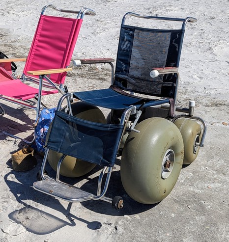 A wheeled chair, I think intended to be pushed by a second person, with enormous front and rear wheels for the sand.  All parts look sand-capable -- the seat and back and leg supports are made of a synthetic-looking mesh that could clearly be hosed down to get the sand/salt off of it.  The wheels have no obvious/easy way for the chair occupant to push them (but on the sand that might take a LOT of force).