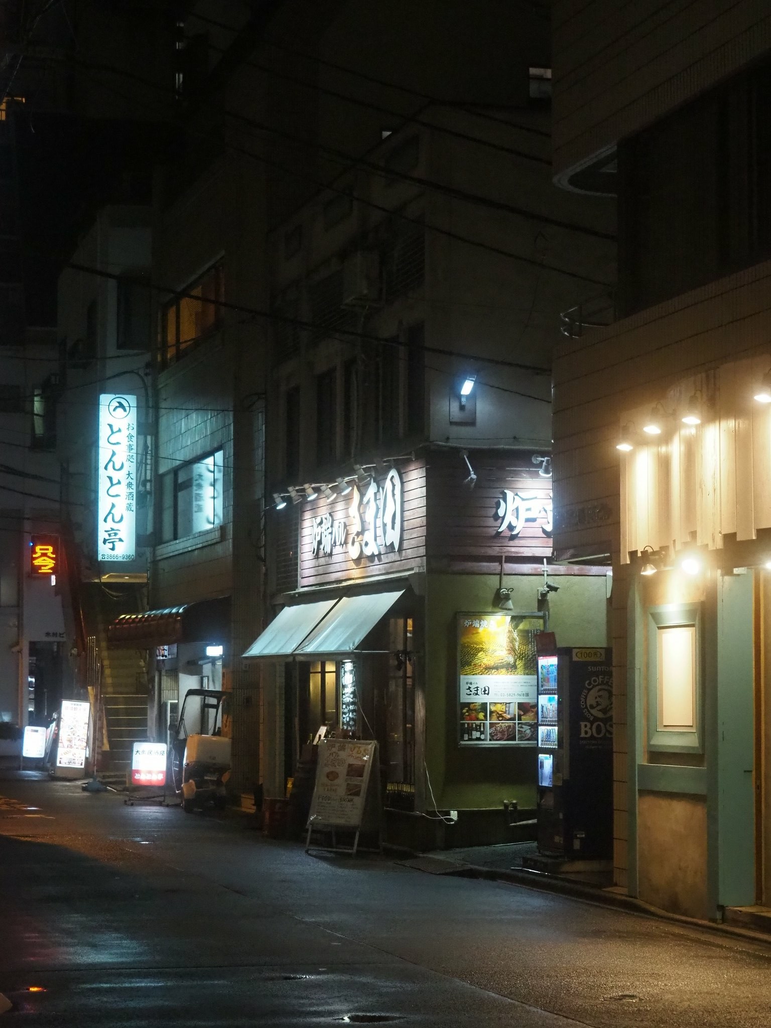 Empty and wet street with glowing signs in Tokyo at night.