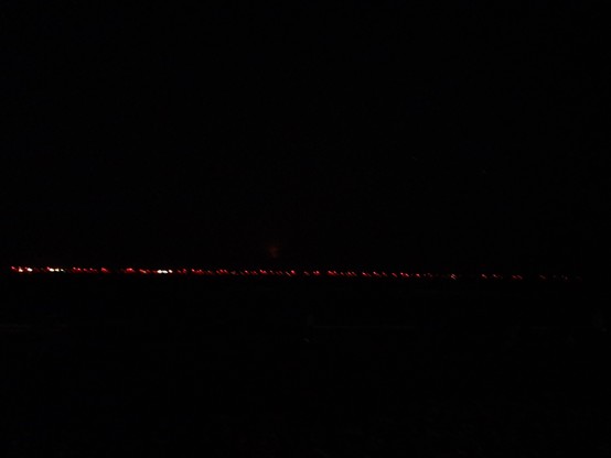 White and red lights from windmills out in the sea. The picture is completely black with a narrow line of red and white dots from windmills and possibly offshore oil rigs all the way across the image.