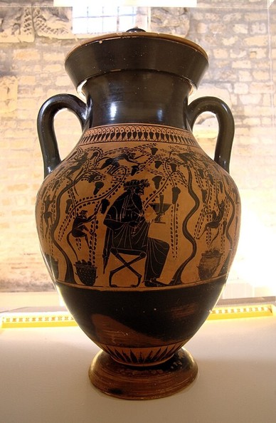 Black figure vase with the god Dionysos sitting on a stool in the shade of vines heavy with grapes.