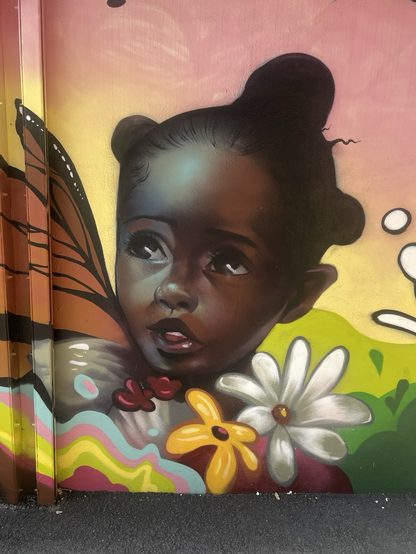 A beautiful dark skinned toddler looks up and to her right. She has monarch butterfly wings and is illumined by an ethereal light.