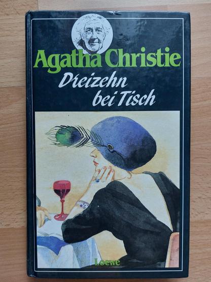 Buch: Agatha Christie: Dreizehn bei Tisch
Eine Aquarellzeichnung eine Frau, die an einem Tisch Sitzt. Der Rücken ist uns zugewandt,  das Gesicht mit einem Hut verdeckt