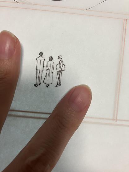 漫画の原稿の写真。
小さな人物が3人描かれている。
大きさの比較のため指が写っている。
小さな人物の絵は全身で2センチくらい。