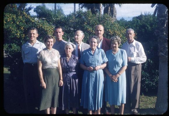 9 of my relatives standing in front of two fruiting calamondin (aka kalamansi) trees, with palm trees in the background and one palm tree truck framing the right edge.  The picture was taken in I think 1953.

Participants L to R, men behind, women in front:
my adopted grandfather (father's uncle) 