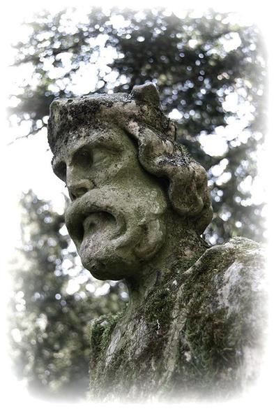 An old weathered statue of a king under trees in a country estate