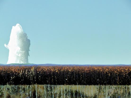 Fountain surging, water spilling over a concrete edge, blue sky behind.  A sorta-abstract picture, something wet and cool on a hot day...