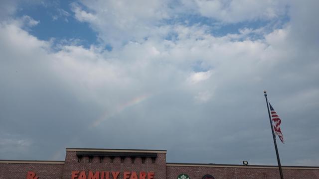 Top edge of a grocery store. Above it, clouds open wide for a rainbow.