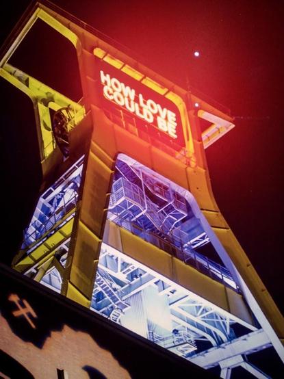 An illuminated industrial structure at night with the words 