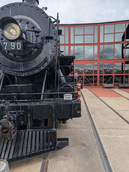 A historic steam engine with the number 790 on it sits in front of a glass windowed roundhouse at the Steamtown National Park