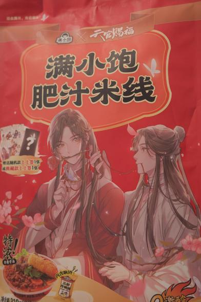 Bag of noodles with two long haired anime guys, one dressed in red, the other dressed in white. The one in white appears to be tying up the hair of the one in red. 