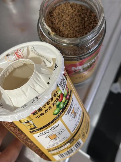 A Nescafé jar filled in with instant cafe in the back. And the container it was in before. You can see the opening of it and the instruction on the side.