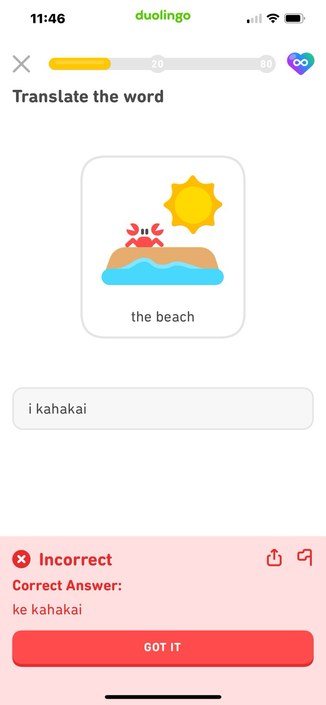 Screenshot from Duolingo. The lesson prompt is a cartoon image of a tan horizontal area representing sand with a wavy blue area beneath representing waves; a red cartoon crab stands atop the sand, and a yellow cartoon sun hangs above. Lesson prompt text: “the beach.” I have answered “i kahakai” but at the bottom is the judgement “Incorrect! Correct answer: ke kahakai” in a bright red box!