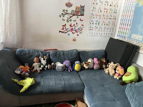 The sofa is covered in stuffed animals and a doll. They sit nearly next to each other. There is no space to sit. 