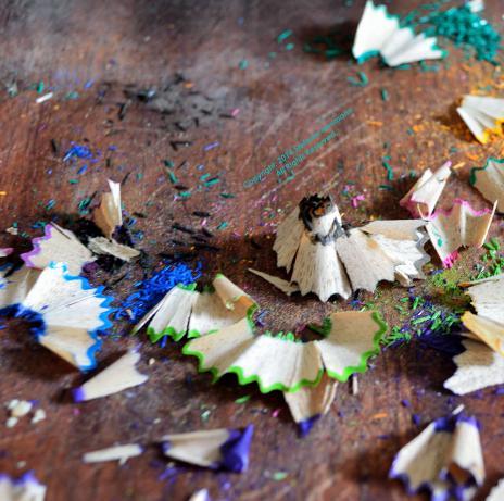 Colourful shavings of coloured pencils on a wooden surface.