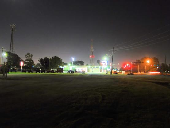 From left:  a cell phone tower, a few trees, looks like some farm equipment, two tractors and a lawnmower.  A highly-lit gasoline station, two sets of stop lights.  

In the foreground, a wasteland of nullity, a truck parking lot.