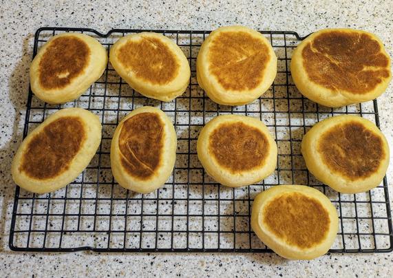 Nine English muffins on a cooling rack on a countertop 