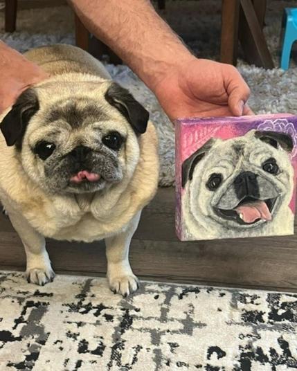 A fawn pug standing next to a painting of a happy fawn pug on a purple and pink gradient background.