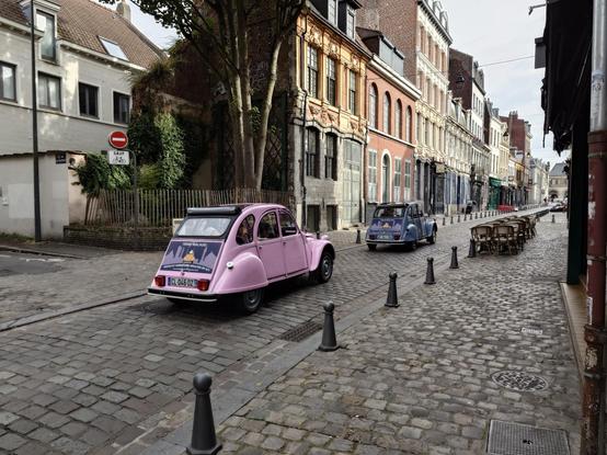 Two Renault 4 cars, one pink and another one blue driving on the old paved street