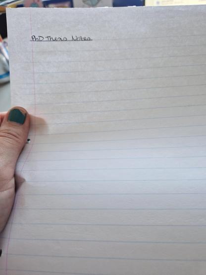 A hand holding a piece of A4 lined paper that is blank other than the handwritten heading 'PhD Thesis Notes'.