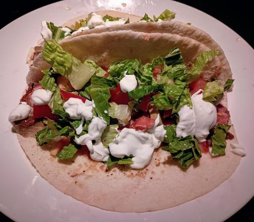 Plate of tacos with one open-faced showing lettuce, tomatoes, and sour cream on top