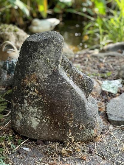 Stone sculpture of a human face in a garden setting.