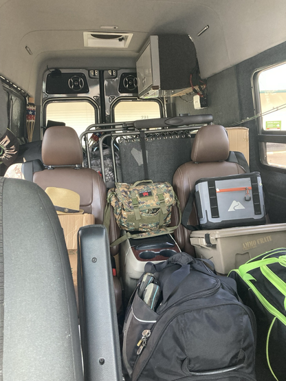 The inside of a cargo van, looking back, piled up with crates and tubs and folding chairs 