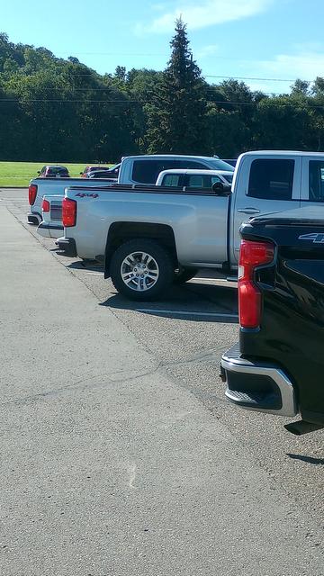 A small 90's white truck with purple gray graphics dwarfed by two newer trucks.