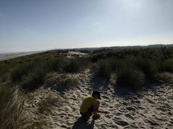 My 10 yo squatting on the sand in front of a dune