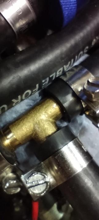 A defective brass tee fitting connected to rubber pipes with a barely visible hole in it.