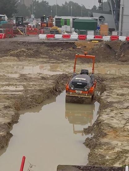 A road roller in a water filled ditch. The water surface is still and reflective.