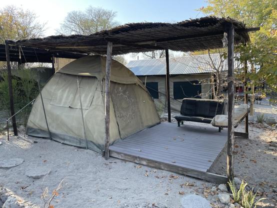 A safari tent with a small terrace and a bench 