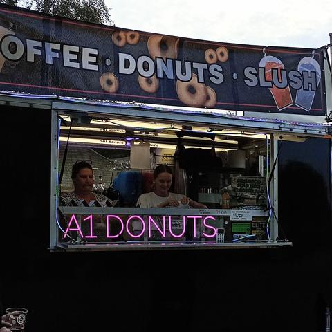 A snack stand selling coffee donuts and slushies. A pink neon sign just below the serving hatch reads A1 DONUTS 