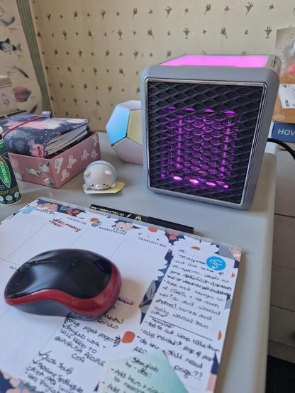 A desk heater, lit from within by a purple light, on a desk with assorted bits of stationery, a tube of Berocca and a wireless mouse on a planner pad