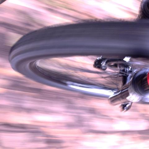 The front wheel of a mountain bike spins over a blurry, leaf covered path.