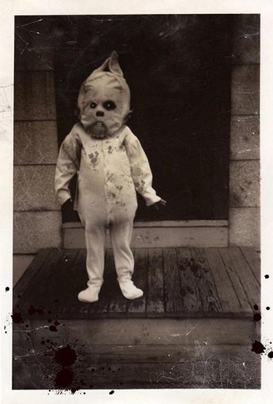 Old sepia photograph of a strange child in a homemade Halloween ghost costume