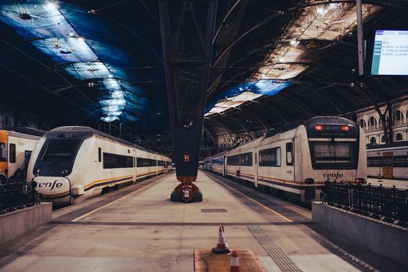 Two Renfe class 448 and 449 medium-distance trains parked at Estació de França, with their lights off. There's a platform between them, where the large metal columns that support the two metallical canopies on the roof sit.