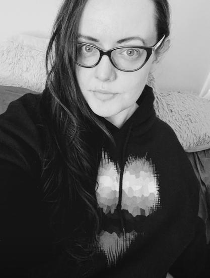 Black and white photo of a white person with long dark hair wearing cat eye glasses and a black sweatshirt