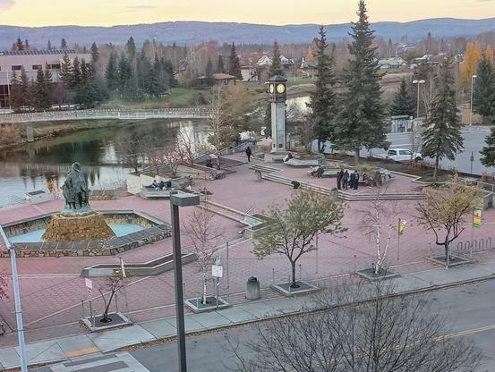 Golden Heart plaza in downtown Fairbanks Alaska, a terraced red brick space on the Chena river with trees, a sculpture of Alaska natives, and a clock tower