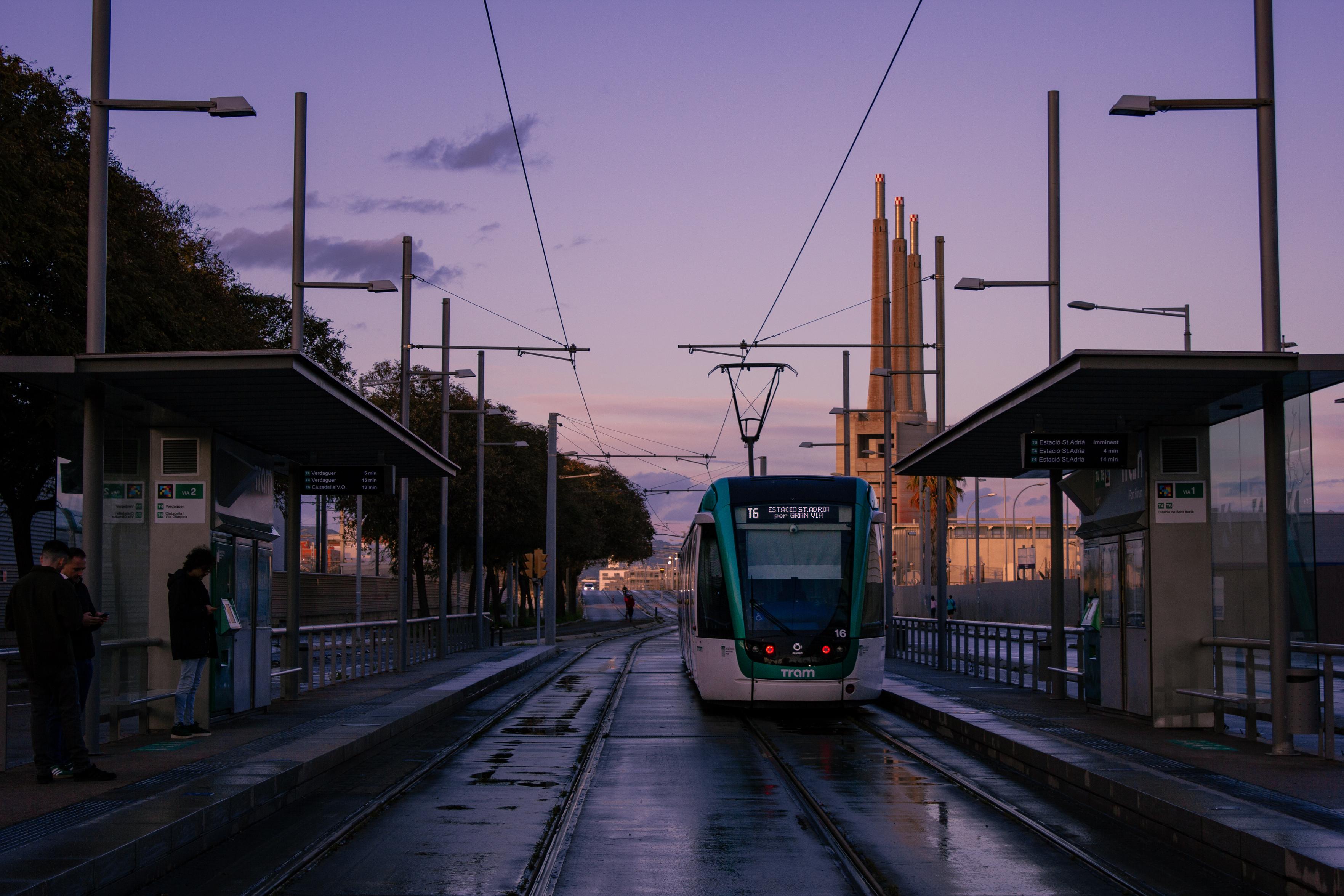 A green Barcelona tramway leaving its stop. The ground underneath is still wet, as it had just rained. At the background, the three chimneys of Sant Adrià can be seen. A green Barcelona tramway leaving its stop. The ground underneath is still wet, as it had just rained. At the background, the three chimneys of Sant Adrià can be seen.