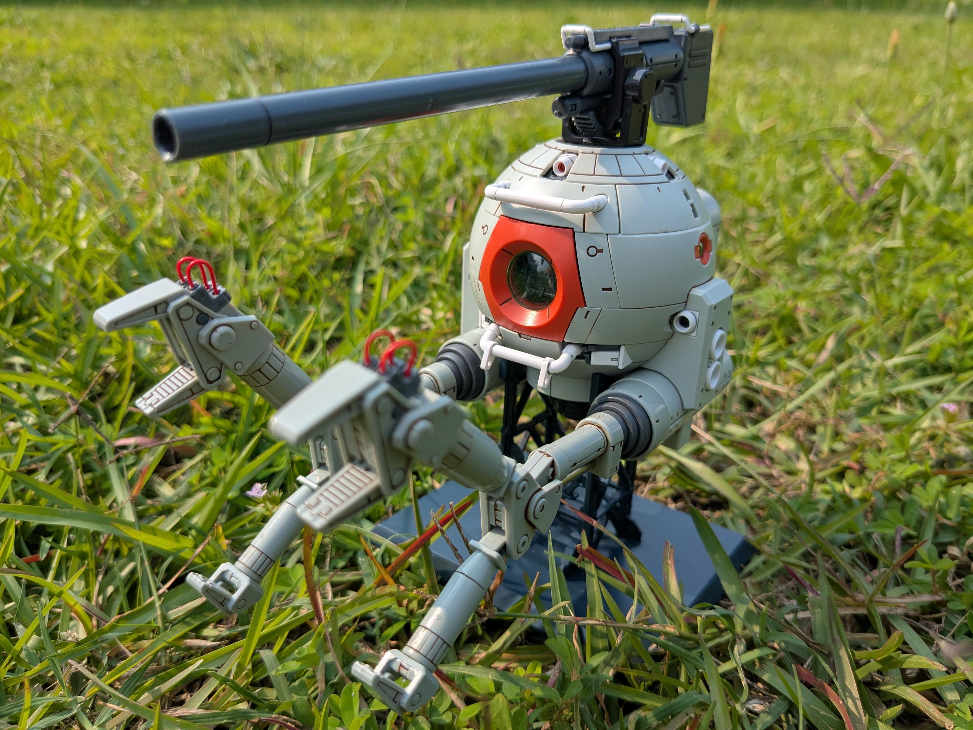 The MG RB-79 Ball on a grassy field. The bottom manipulators on each arm have been extended. It is facing far left of the viewer.