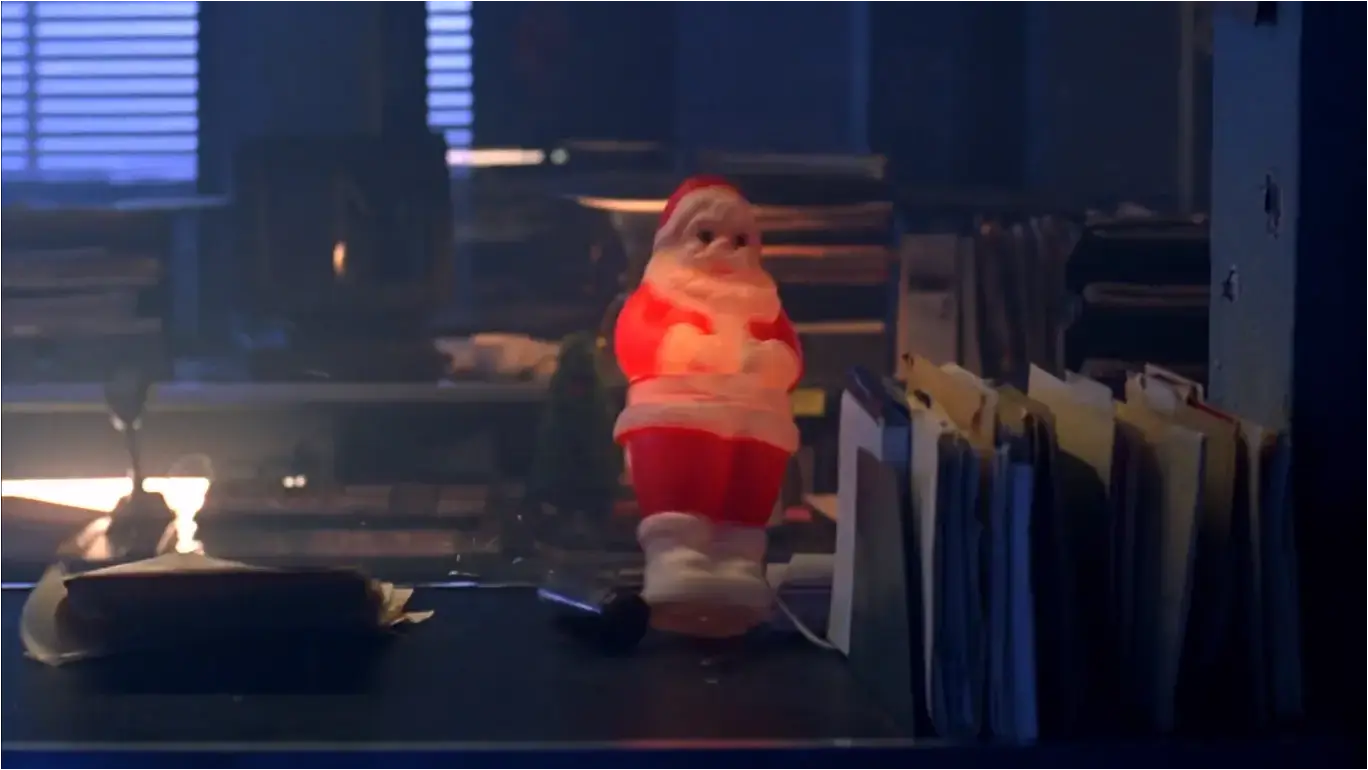 Screenshot from the film &#39;The Minion&#39; (2016) - A desktop in a police station, on it files, a lamp &amp; a small illuminated plastic Santa Claus toppling over from a gunshot
