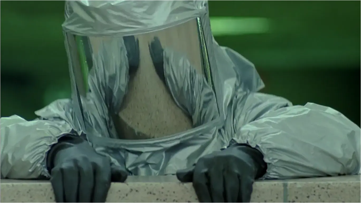 Screenshot from the film &#39;The Minion&#39; (2016)- The hero wearing a silver hazmat suit, grey gloves &amp; a full-head helmet with mirrored glass (thus the face not visible) pulling himself up over a wall.