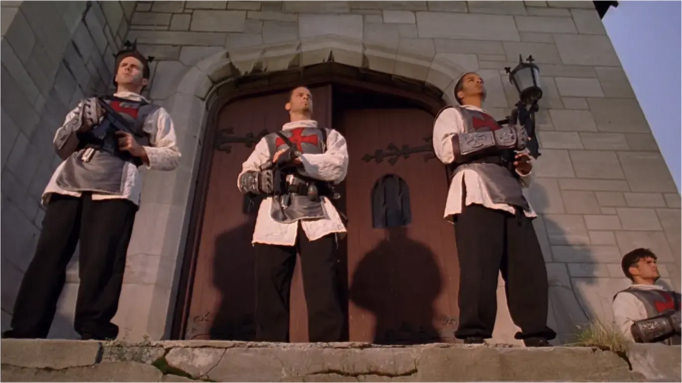 Screenshot from the film &#39;The Minion&#39; (2016) - Upward-looking view of 4 Knights Templar standing in front of church doors looking outward on guard, machine pistols at the ready.