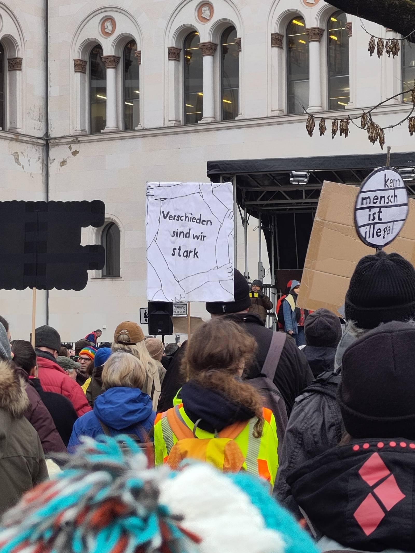 Demoszene Richtung Bühne fotografiert. Im Zentrum ist ein hochgehaltenes Schild mit dem Text "verschieden sind wir stark"