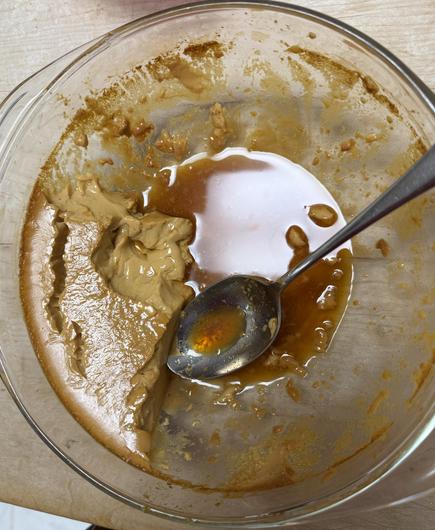 A pyrex bowl containing a mostly-eaten flan, with some caramel syrup still in the bottom, and the flan itself somewhat caramel-colored.  A sticky spoon rests in the bowl.