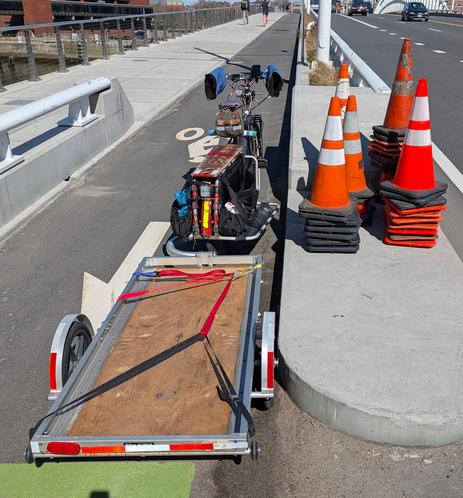 A big dummy bicycle with trailer attached, next to five stacks of Awareness Cones, to be loaded onto the trailer.

The bike is pointed wrong-way in the bike lane on the Washington Street Bridge over the Charles River in Boston.  It got moved before loading, but the bike lane is also not busy.