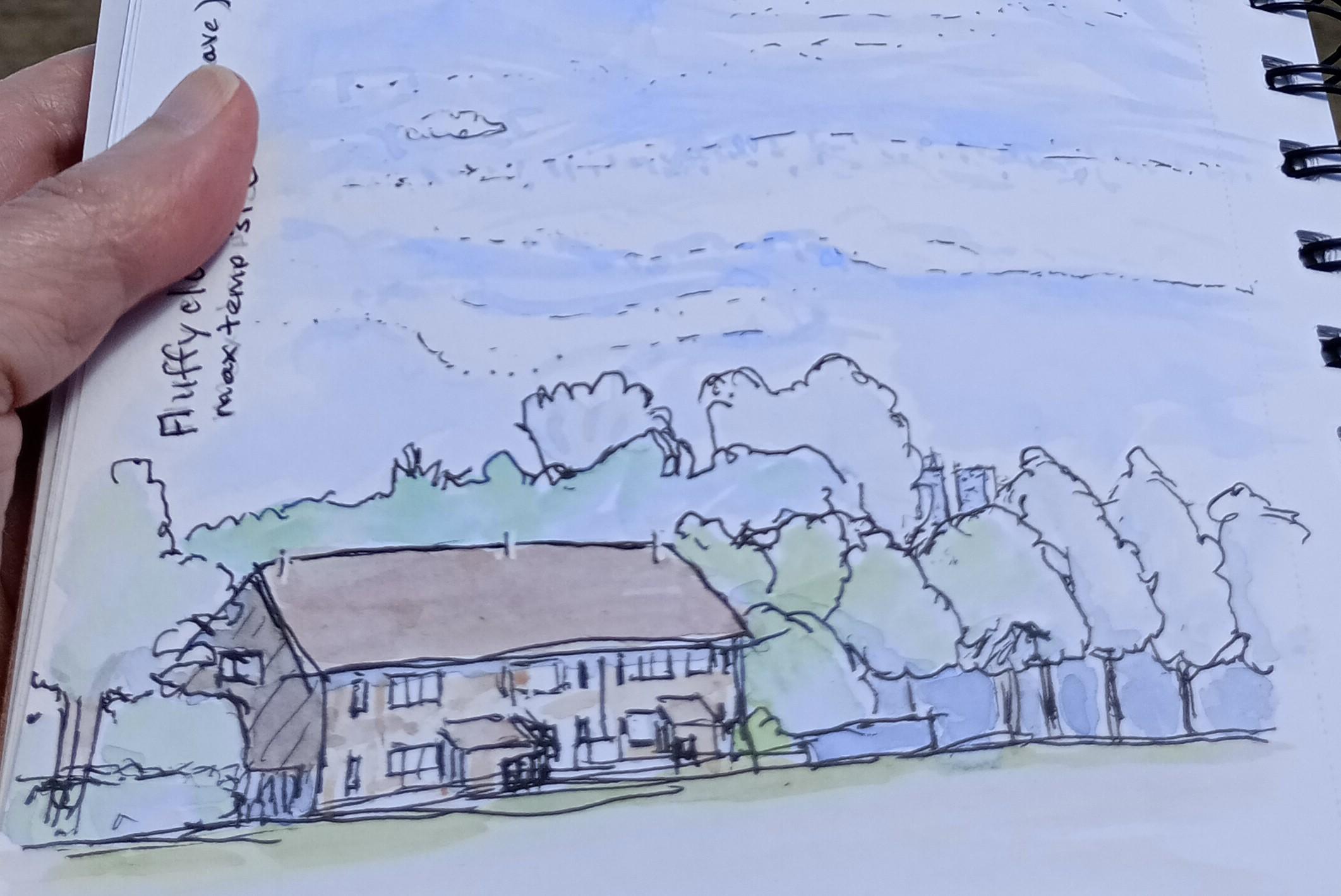 A hand holding a spiral bound sketch book with a watercolour painted scene of a row of houses and trees.